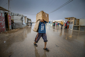 A young Syrian refugee shelters from the rain with a cardboard box. Extreme weather - from sandstorms to thunderstorms - are a common occurence in UNHCR Zaatari refugee camp and make life difficult for the people living there.